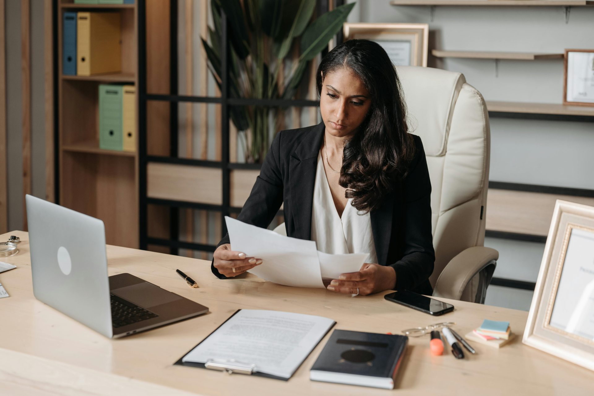 Mujer de negocios concentrada en el papeleo en el escritorio de la oficina, revisando documentos.